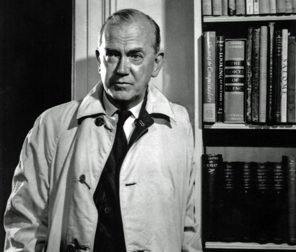Retrato de Graham Greene con gabardina junto a una biblioteca