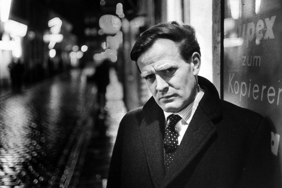 Foto de John le Carré junto a un letrero en alemán